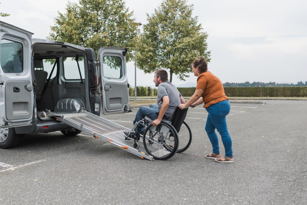 A woman pushes a man in a wheelchair towards a van